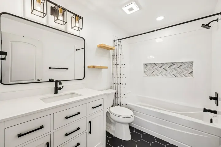 Bathroom featuring a white vanity with integrated sink, black hexagonal floor tiling, and a tub with a tiled niche