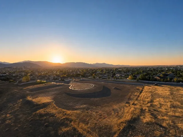 Expansive undeveloped land with a gradual slope, bordered by a paved roadway and established residential properties