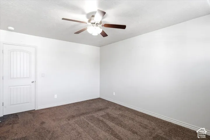 Neutral wall paint, brown carpet flooring, ceiling fan with light fixture, and a white paneled door