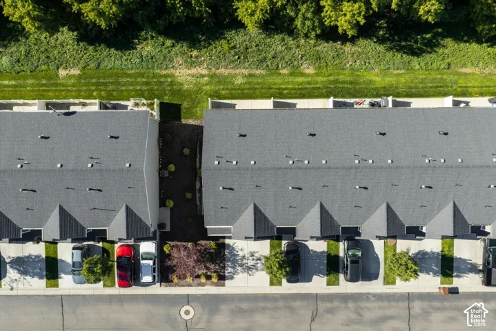 Row of residences with dark shingle roofs, individual driveway parking, and a manicured green space bordering the rear