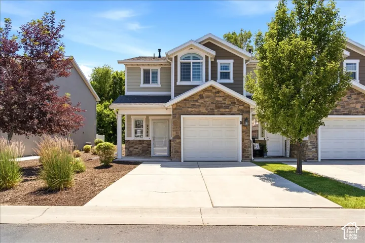 Two-story residence featuring a stone and siding facade, covered front entry, arched window, and an attached two-car garage