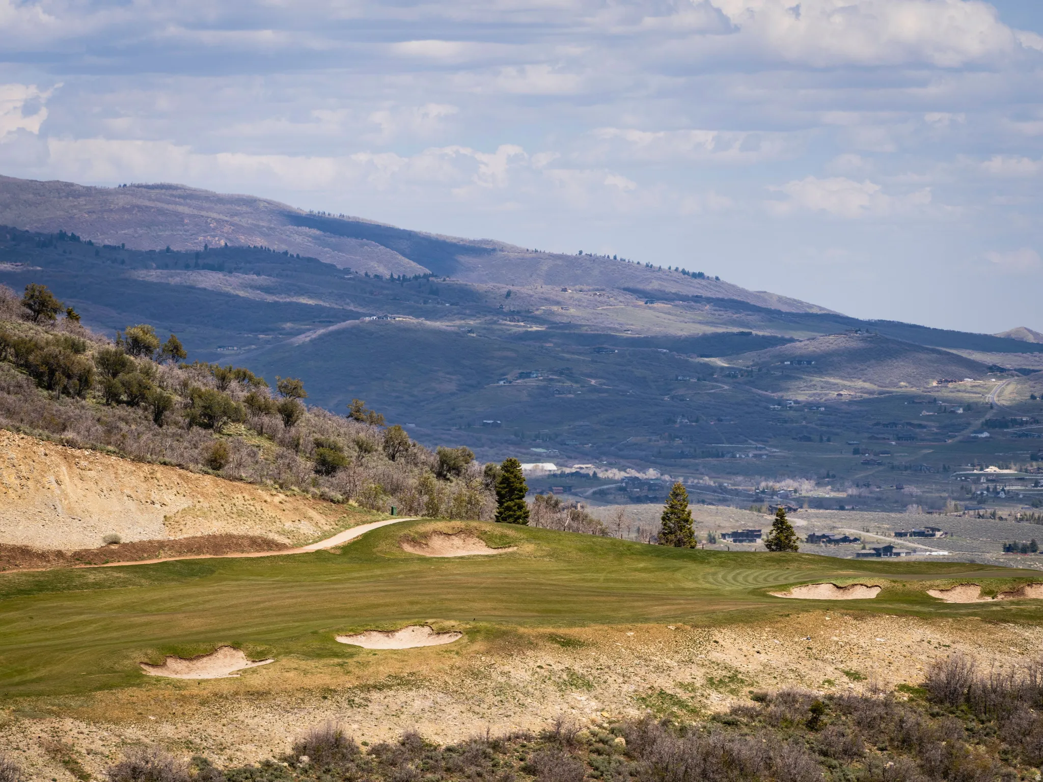 Manicured golf course green with sand traps, bordered by a hillside with varied vegetation