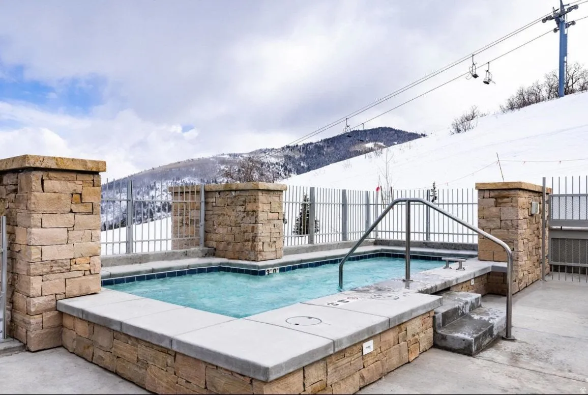 Outdoor hot tub featuring stone-clad surround, tiled interior, metal handrails, and integrated steps