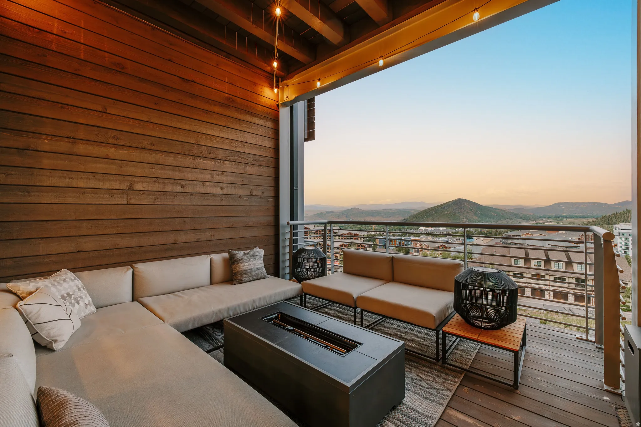Spacious balcony featuring a wood-plank accent wall, overhead string lighting, and a metal railing system