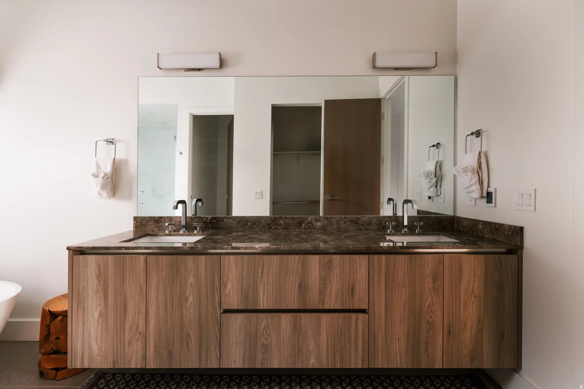 Dual vanity with integrated sinks, a dark patterned countertop, wood-finish cabinetry, and an expansive mirror