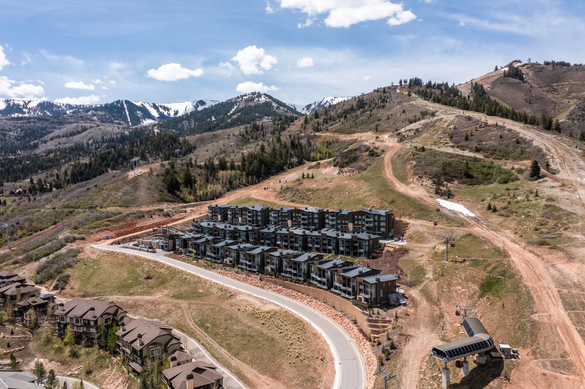 Expansive mountain landscape featuring multiple multi-story residential buildings with contemporary facades, paved roadways, and a ski lift structure