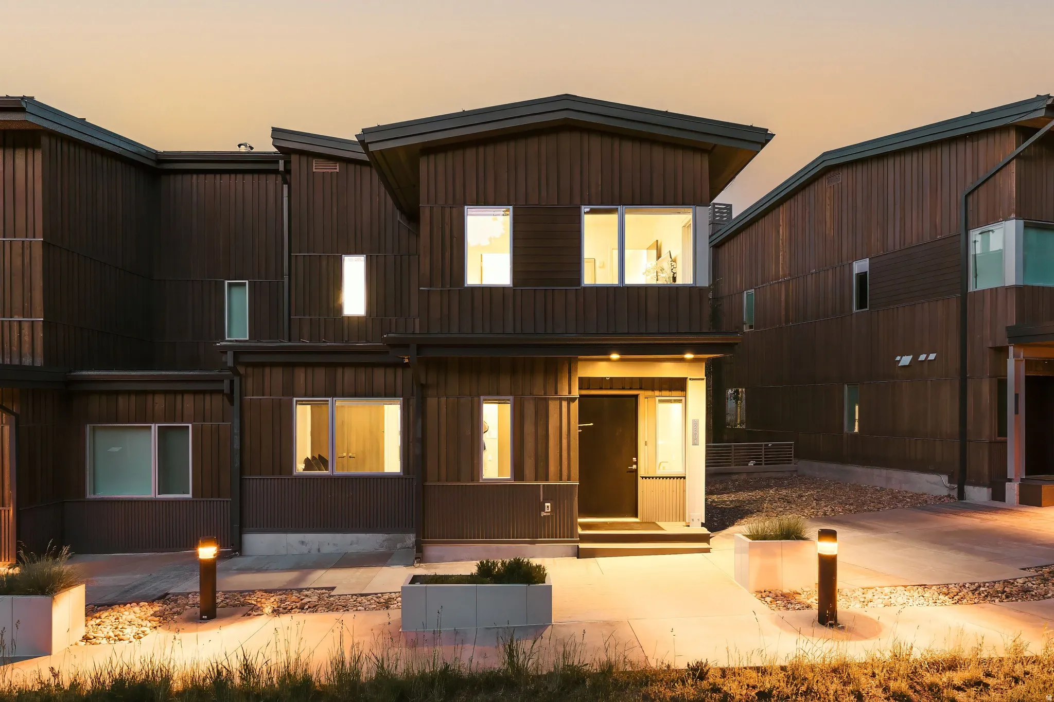 Modern exterior featuring dark wood paneling, a recessed entry, contemporary outdoor lighting, a flat roofline, and multiple windows