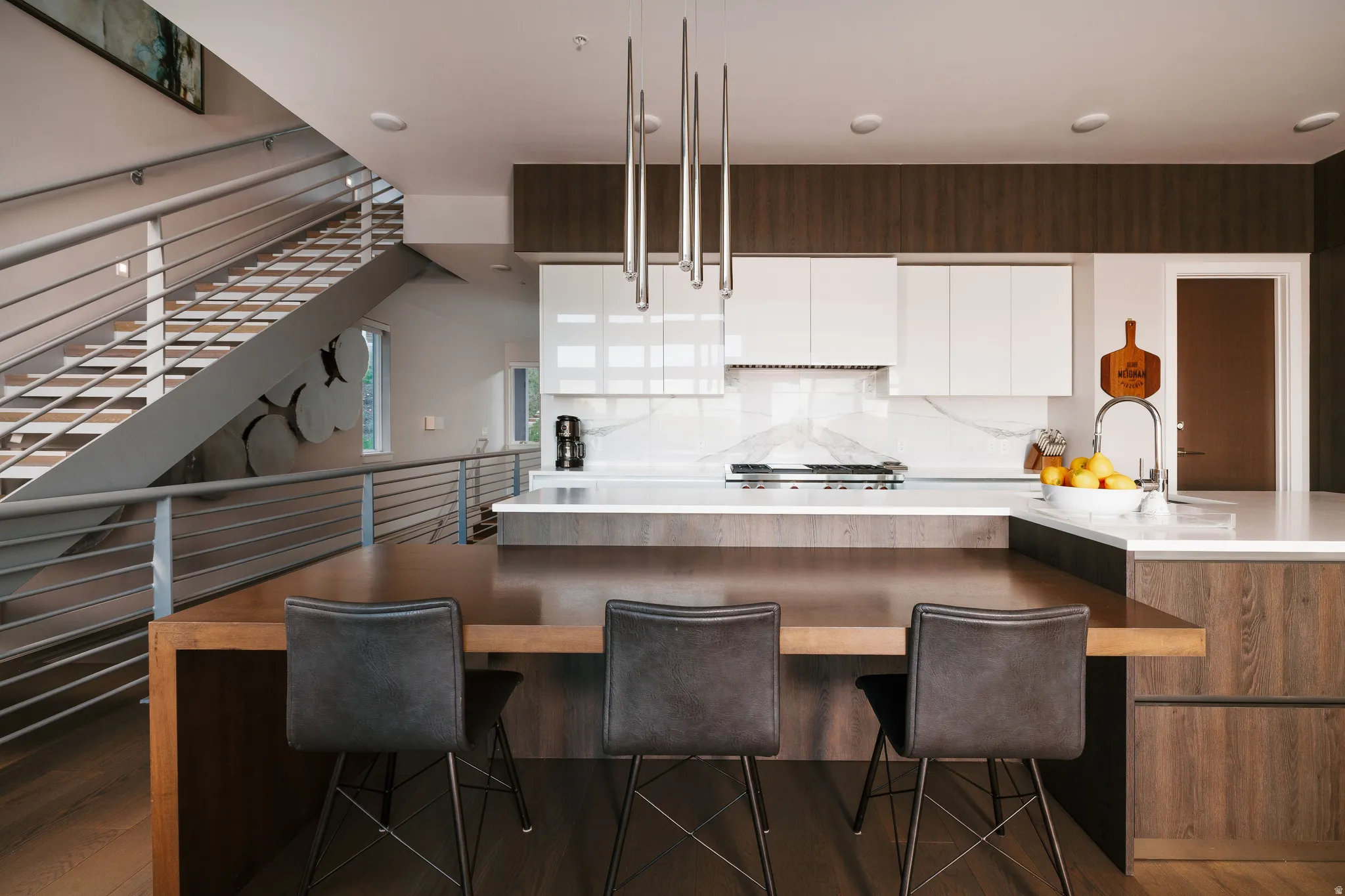 Contemporary kitchen featuring a large island with integrated wood-finish dining surface, white upper cabinetry, and dark wood-finish lower cabinetry
