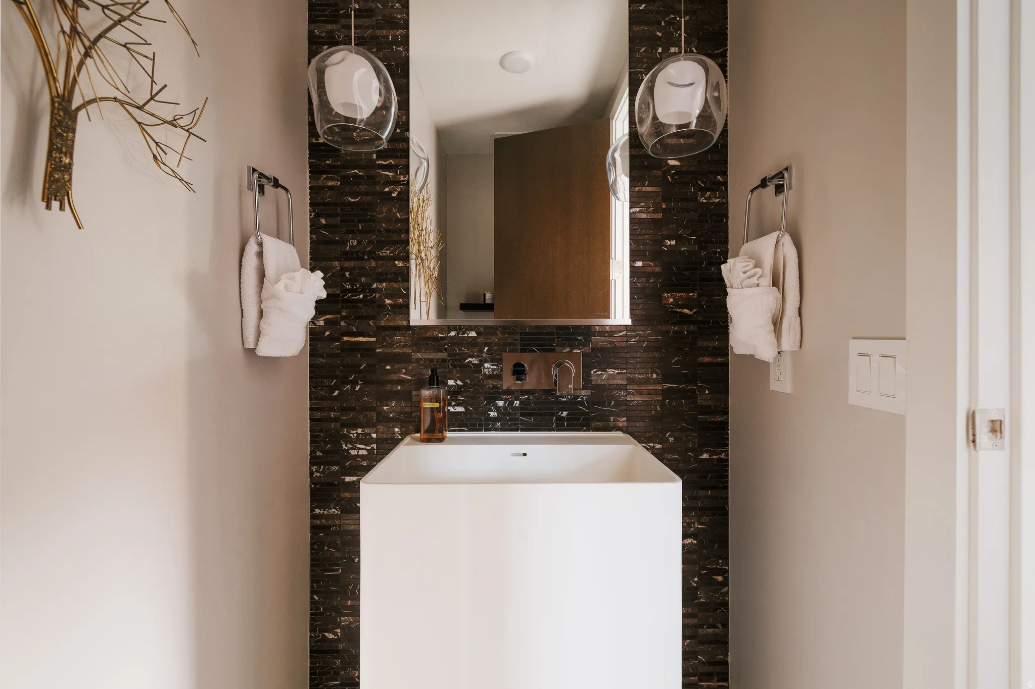 Contemporary bathroom featuring a pedestal sink, wall-mounted faucet, and a dark mosaic tile backsplash