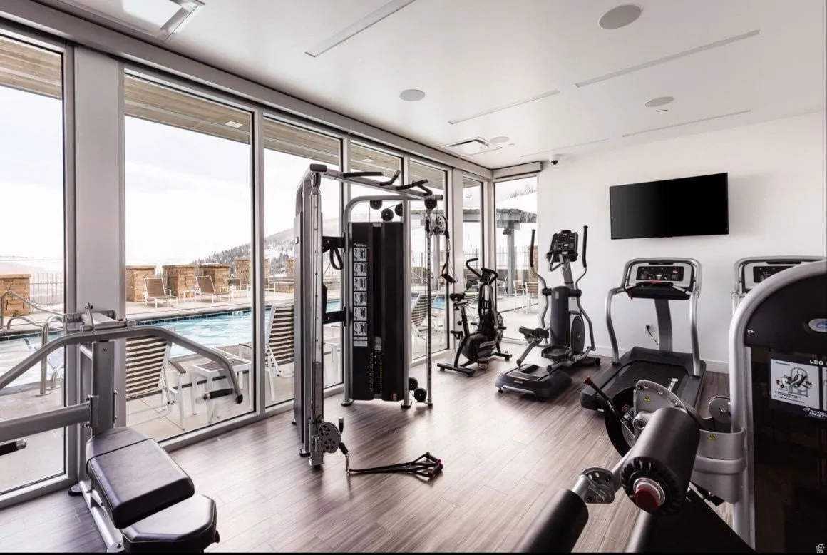 Fitness center featuring floor-to-ceiling windows, wood-finish flooring, recessed lighting, and a wall-mounted display