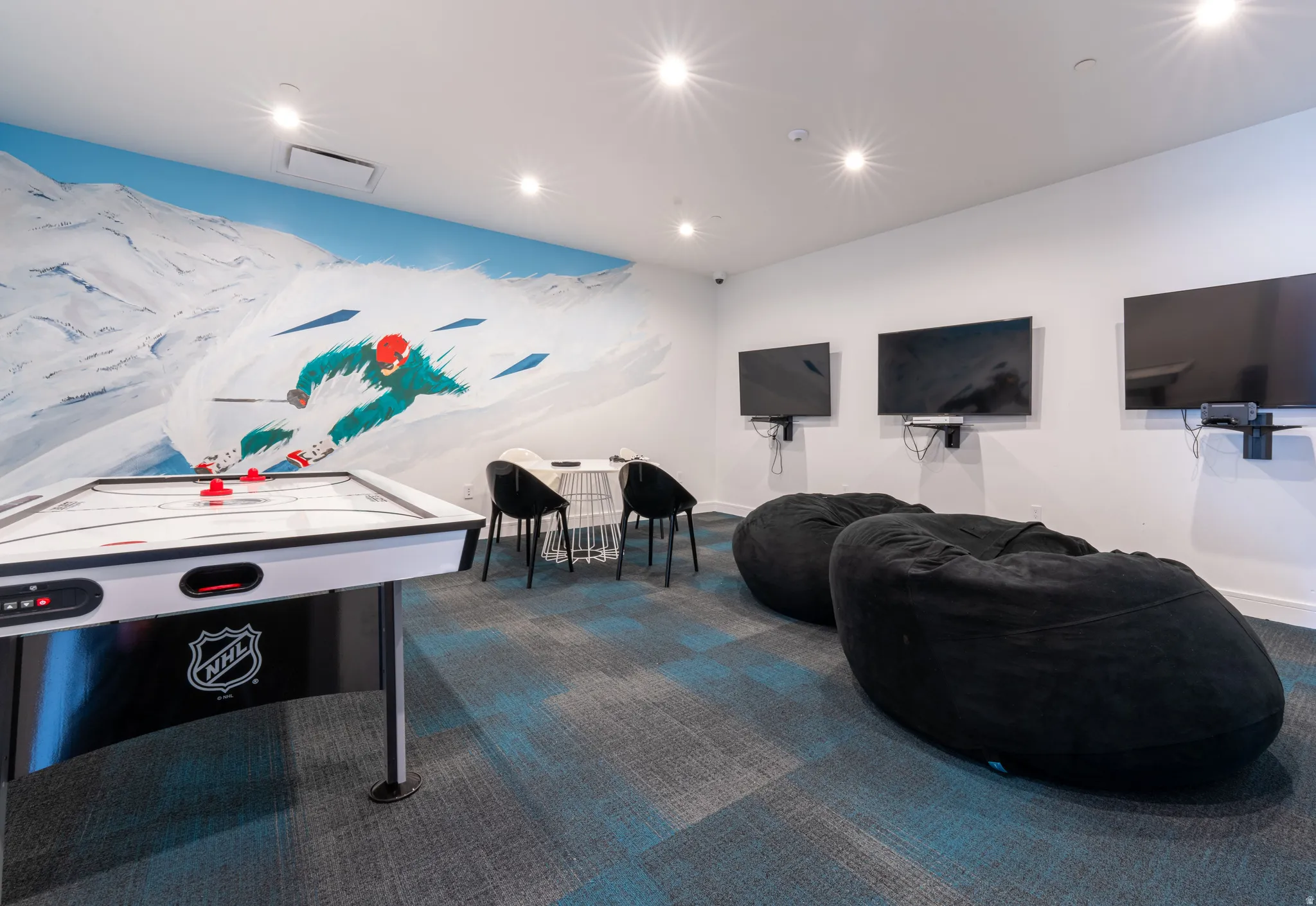 Recreational room featuring an air hockey table, a custom ski mural, patterned carpeting, three wall-mounted displays, and recessed lighting