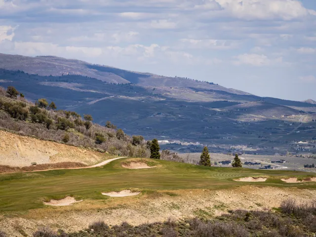 Manicured golf course green with sand traps, bordered by a hillside with varied vegetation