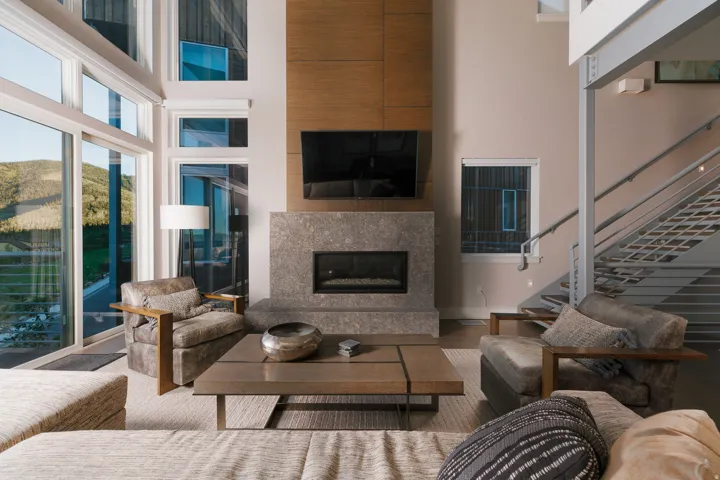 Living area featuring a floor-to-ceiling window wall, a stone-clad fireplace with a wood-finish accent wall, and a multi-level staircase with metal railings