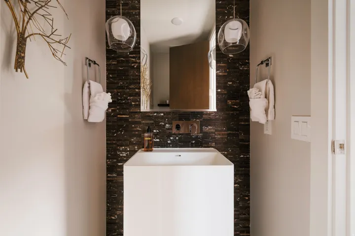 Contemporary bathroom featuring a pedestal sink, wall-mounted faucet, and a dark mosaic tile backsplash