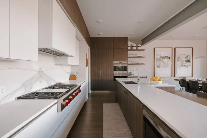 Contemporary kitchen featuring a built-in range, white upper cabinetry, and a full-height marble-finish backsplash