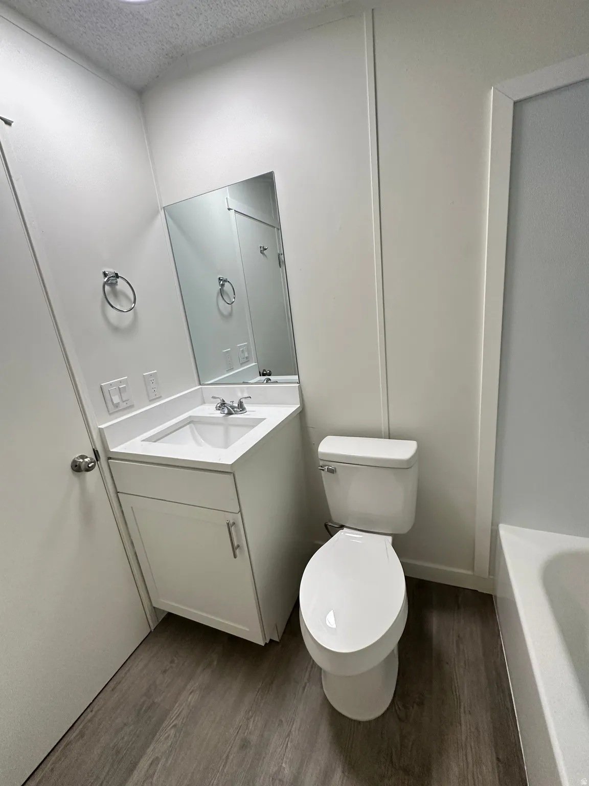 Bathroom featuring a white vanity with a rectangular sink, a wall-mounted mirror, and wood-finish flooring
