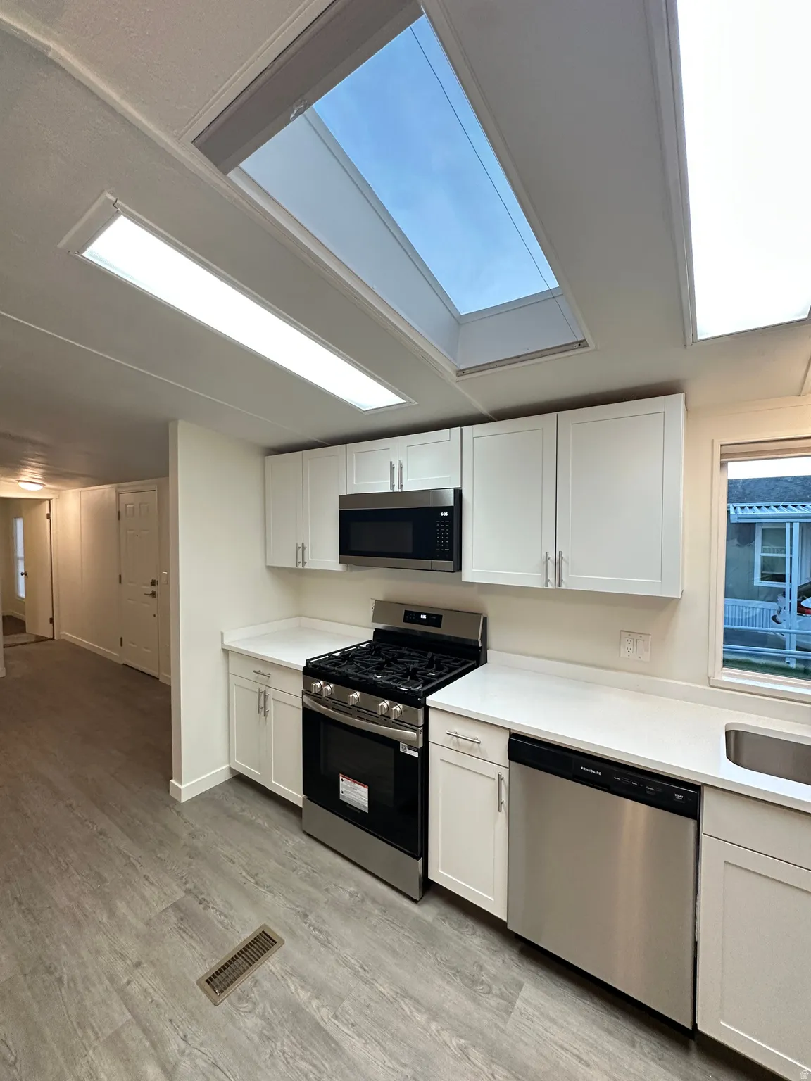 Kitchen featuring a skylight, white cabinetry, stainless steel appliances, white countertops, and wood-finish flooring