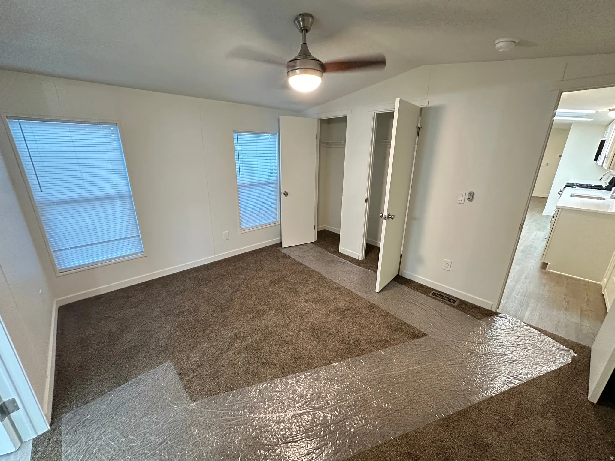 Carpeted room featuring two windows with blinds, a ceiling fan with light fixture, and two closet openings