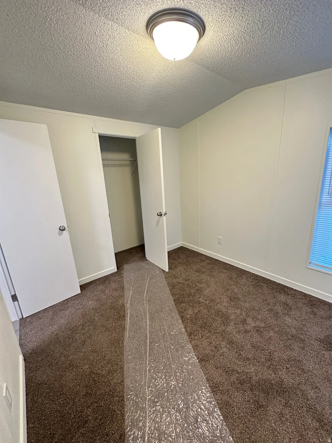 Bedroom featuring textured ceiling, flush mount lighting, a built-in closet, neutral wall paneling, and brown carpeting