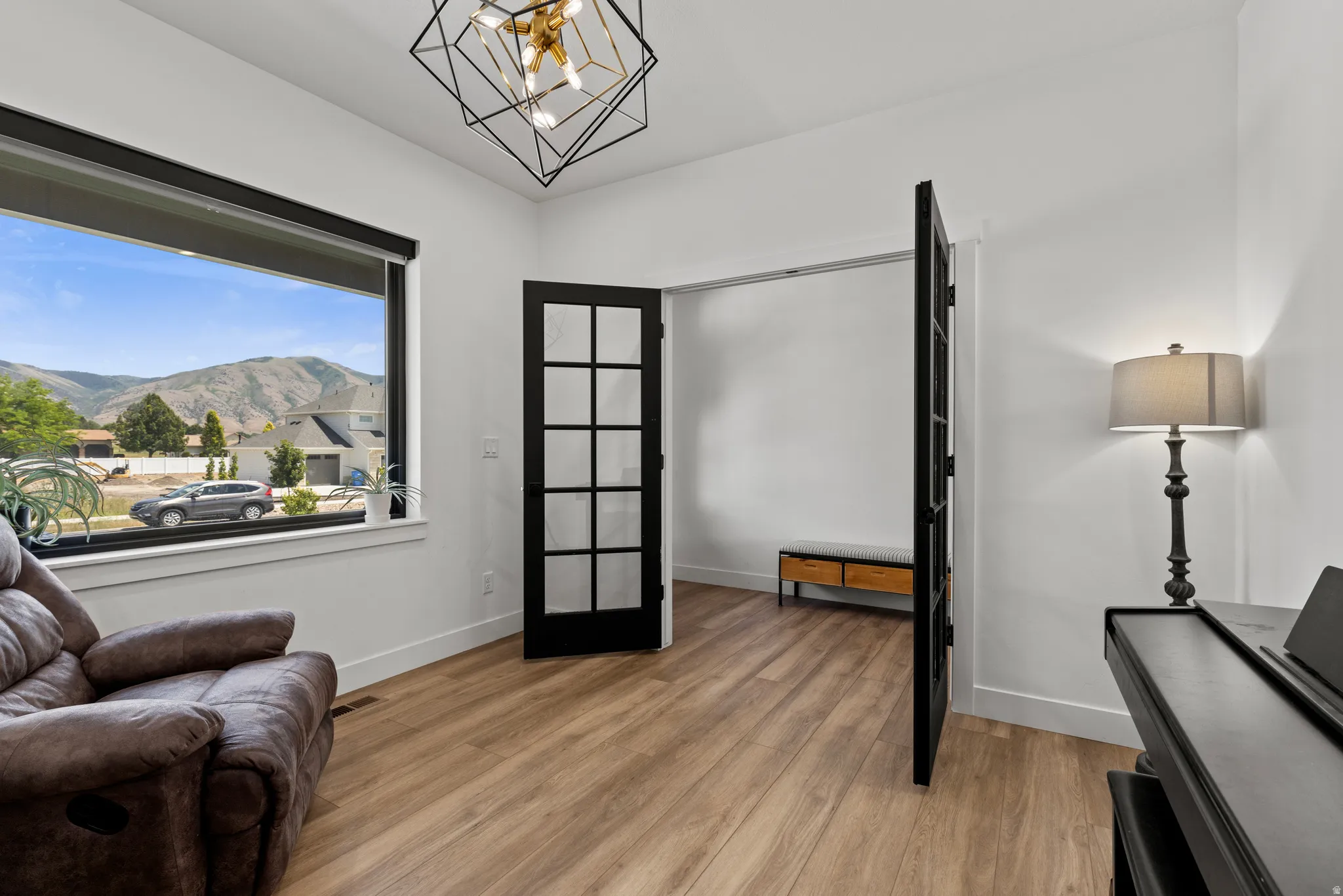 Spacious room featuring a large window, mountain scenery, light wood-finish flooring, and a modern geometric light fixture