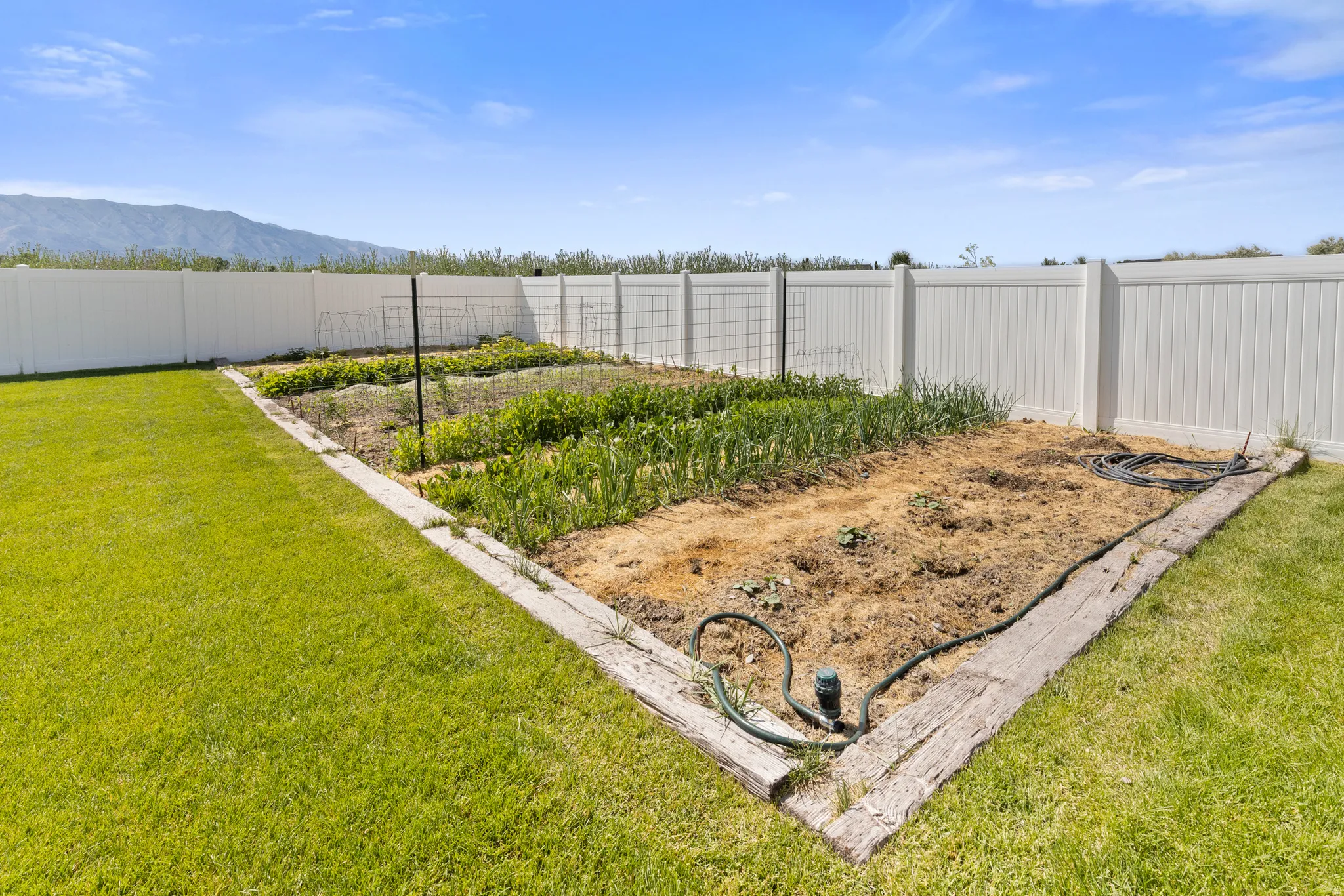Expansive garden plot with wood-look borders, surrounded by a white privacy fence