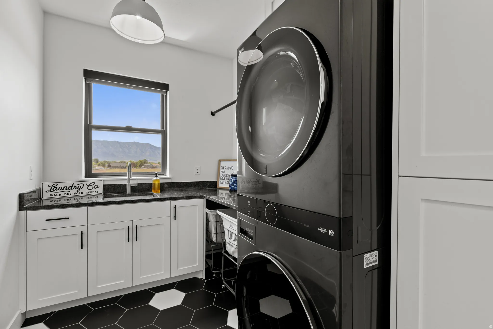 Laundry area featuring a stackable washer and dryer, black hexagon tile flooring, white shaker cabinetry, dark countertops, and a window overlooking a mountain landscape