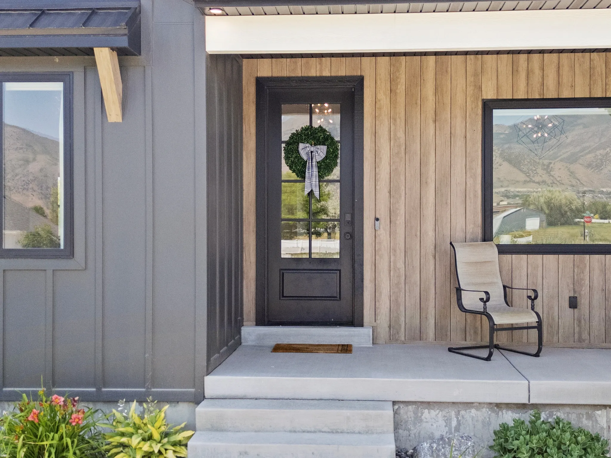 Modern exterior featuring a dark-paneled entry door with glass, a concrete porch, and a combination of vertical wood-finish siding and dark board-and-batten siding