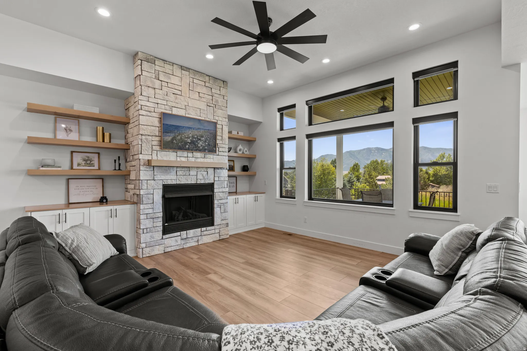 Spacious living area featuring a stone fireplace with a wood mantle, built-in shelving and cabinetry, recessed lighting, and wood-finish flooring