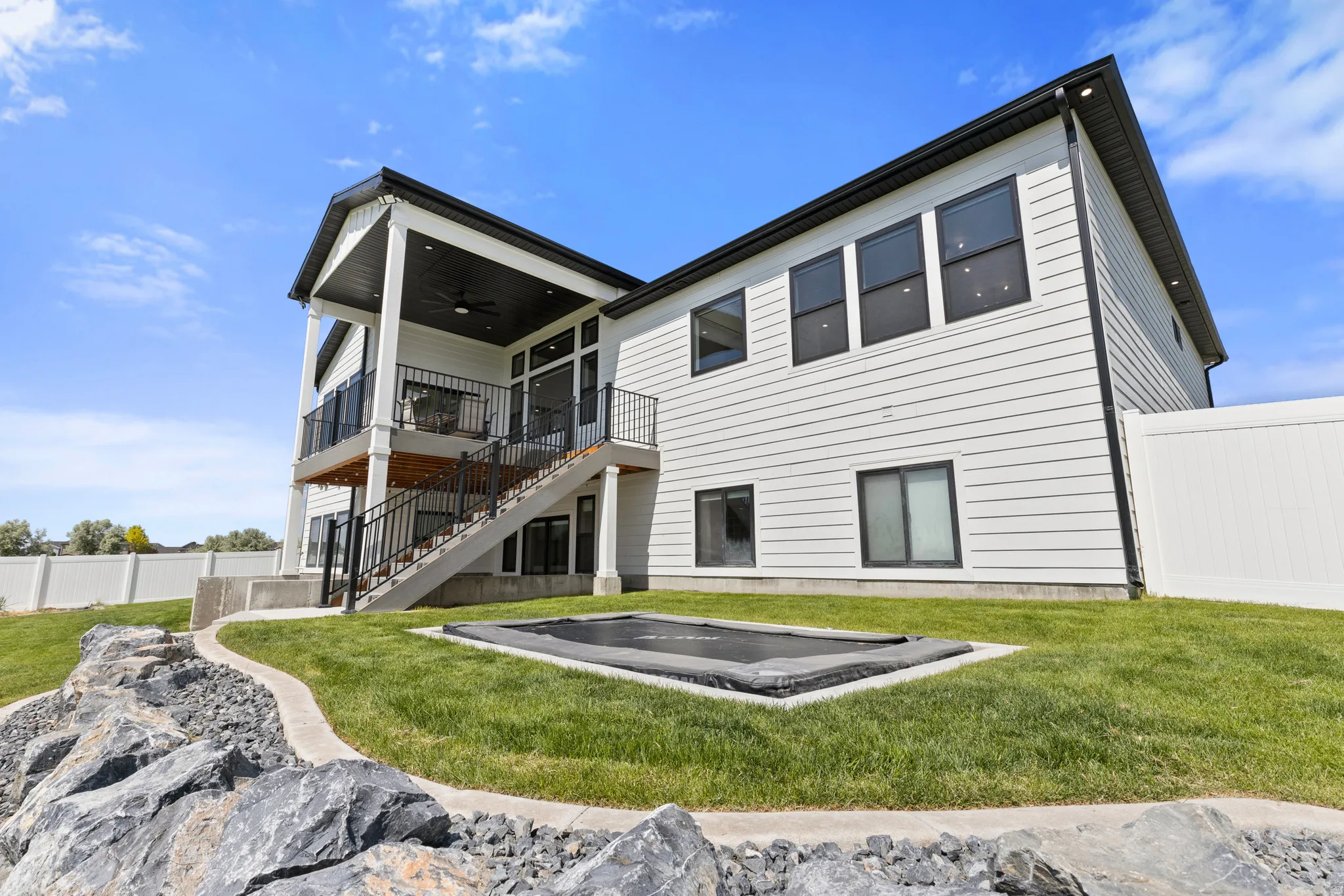 Contemporary exterior featuring white siding with black trim, a covered upper-level deck, a lower-level patio, and a fully fenced yard