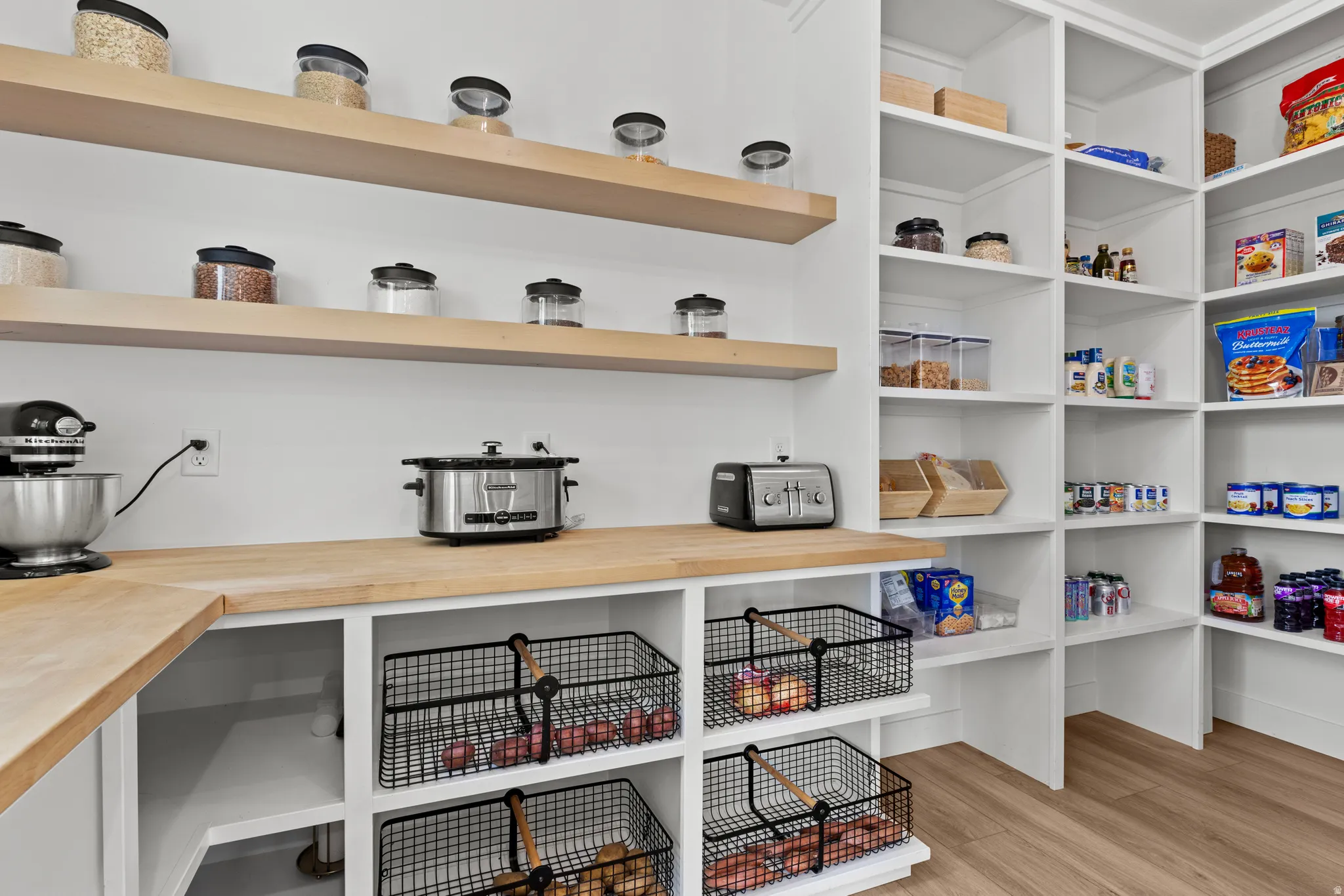 Spacious pantry featuring extensive built-in shelving, natural wood-finish countertops, and integrated wire basket storage