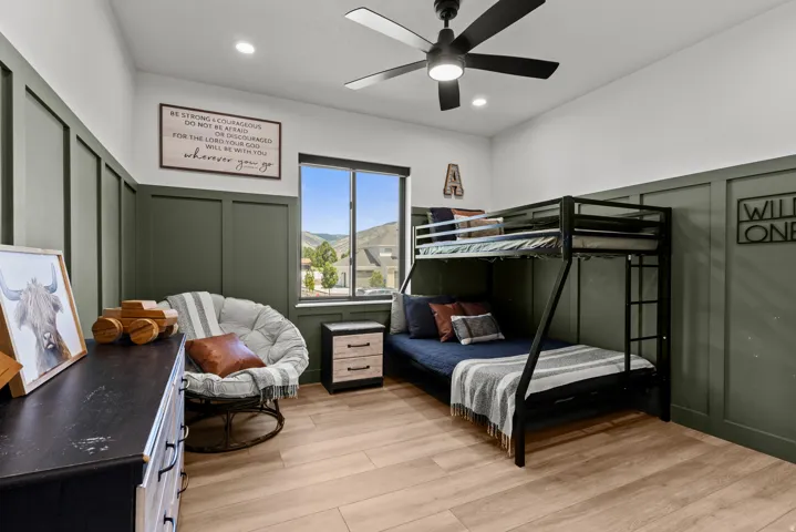 Room featuring light wood-finish flooring, accent wall paneling, a ceiling fan, and a window with mountain scenery