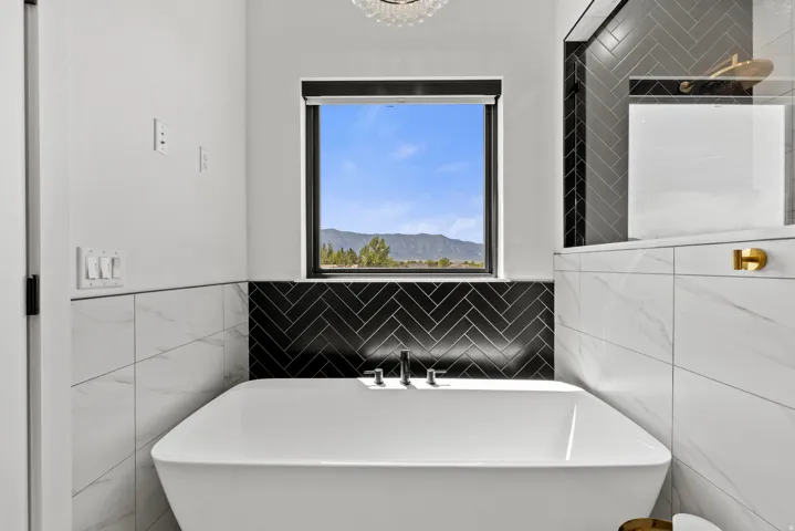 Freestanding soaking tub with mountain scenery through a picture window, complemented by black herringbone tile and white marble-look wall tiles