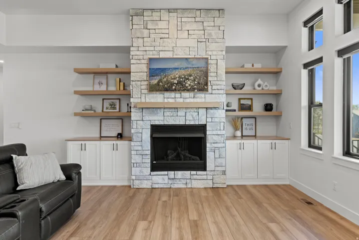 Stone-faced fireplace with a wood mantel, flanked by built-in cabinetry and floating wood shelving