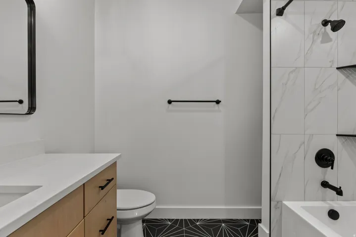 Bathroom featuring a light wood-finish vanity with a white countertop and undermount sink, a sleek black-framed mirror, and matte black hardware