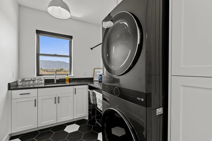 Laundry area featuring a stackable washer and dryer, black hexagon tile flooring, white shaker cabinetry, dark countertops, and a window overlooking a mountain landscape