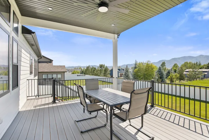 Spacious covered deck featuring composite decking, black metal railings, a ceiling fan, and recessed lighting, all overlooking a mountain range