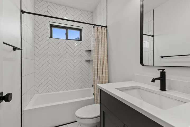 Bathroom featuring a white subway tile shower surround in a herringbone pattern with built-in shelving, a single vanity with a white countertop and integrated sink, a rectangular mirror with a black frame, and matte black fixtures throughout