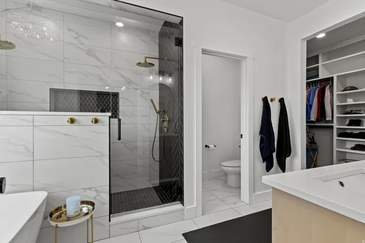 Spacious bathroom featuring a glass-enclosed shower with dual showerheads, a built-in shower niche, and black hexagon tile flooring