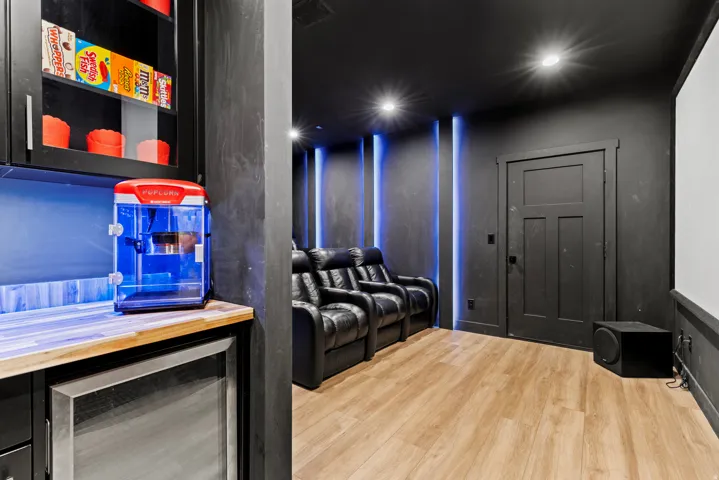 Dedicated entertainment room featuring three leather reclining seats, wood-finish flooring, and recessed ceiling lighting