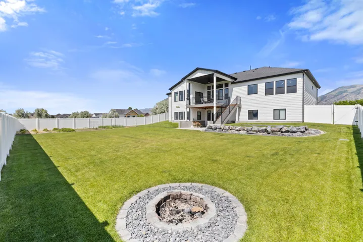 Spacious backyard featuring a manicured lawn, a built-in fire pit with stone and gravel surround, and a white vinyl privacy fence