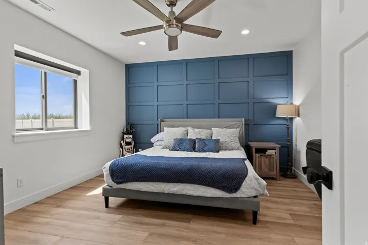 Room featuring a striking blue accent wall with panel molding, light wood-finish flooring, and a ceiling fan with integrated lighting