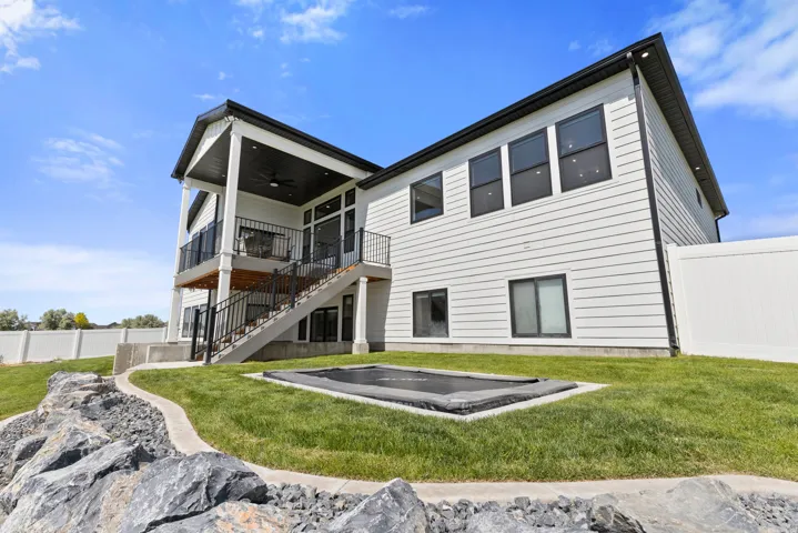 Contemporary exterior featuring white siding with black trim, a covered upper-level deck, a lower-level patio, and a fully fenced yard