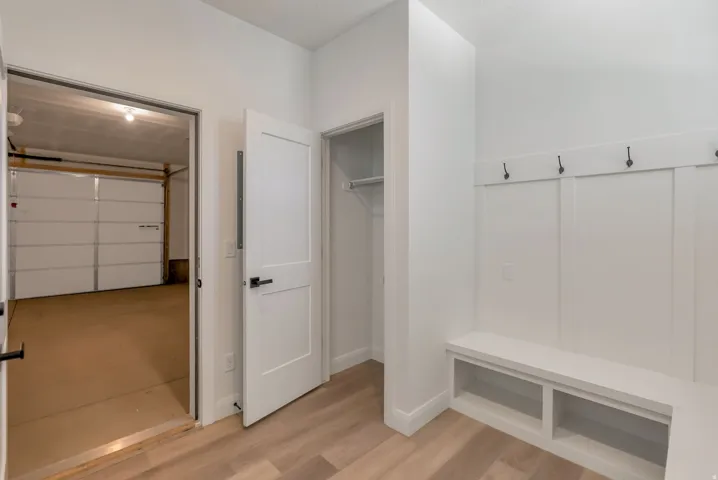 Mudroom area featuring built-in bench seating with storage cubbies, a coat rack with four hooks, and wood-finish flooring