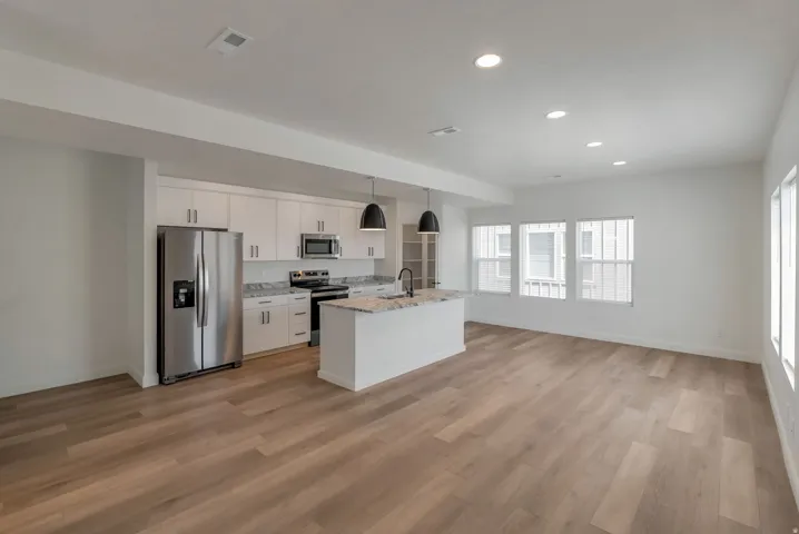 Open-concept living space featuring wood-finish flooring, recessed lighting, and multiple windows with vertical blinds