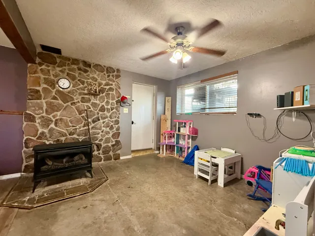 Living area featuring a stone accent wall with an electric fireplace, exposed wood beam, ceiling fan, and a light-colored entry door