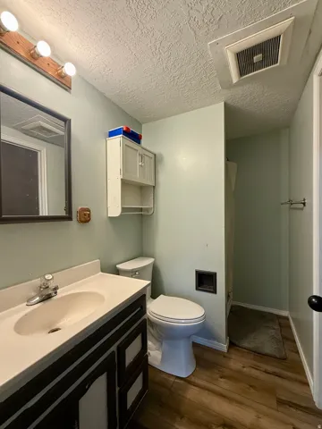 Bathroom featuring a single vanity with a white countertop and dark wood-finish cabinetry, a standard toilet, and wood-finish flooring