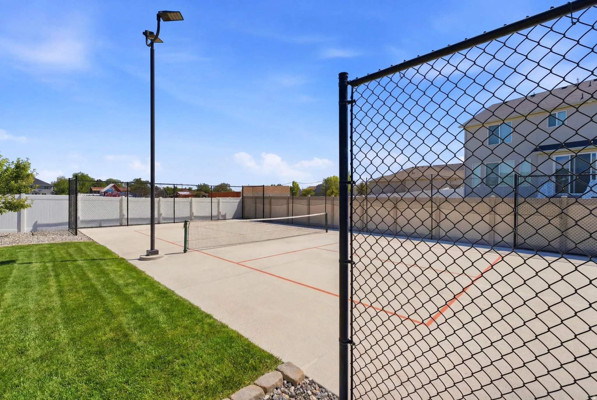 Outdoor sport court featuring a concrete surface with painted lines, black chain-link fencing, and an overhead light fixture