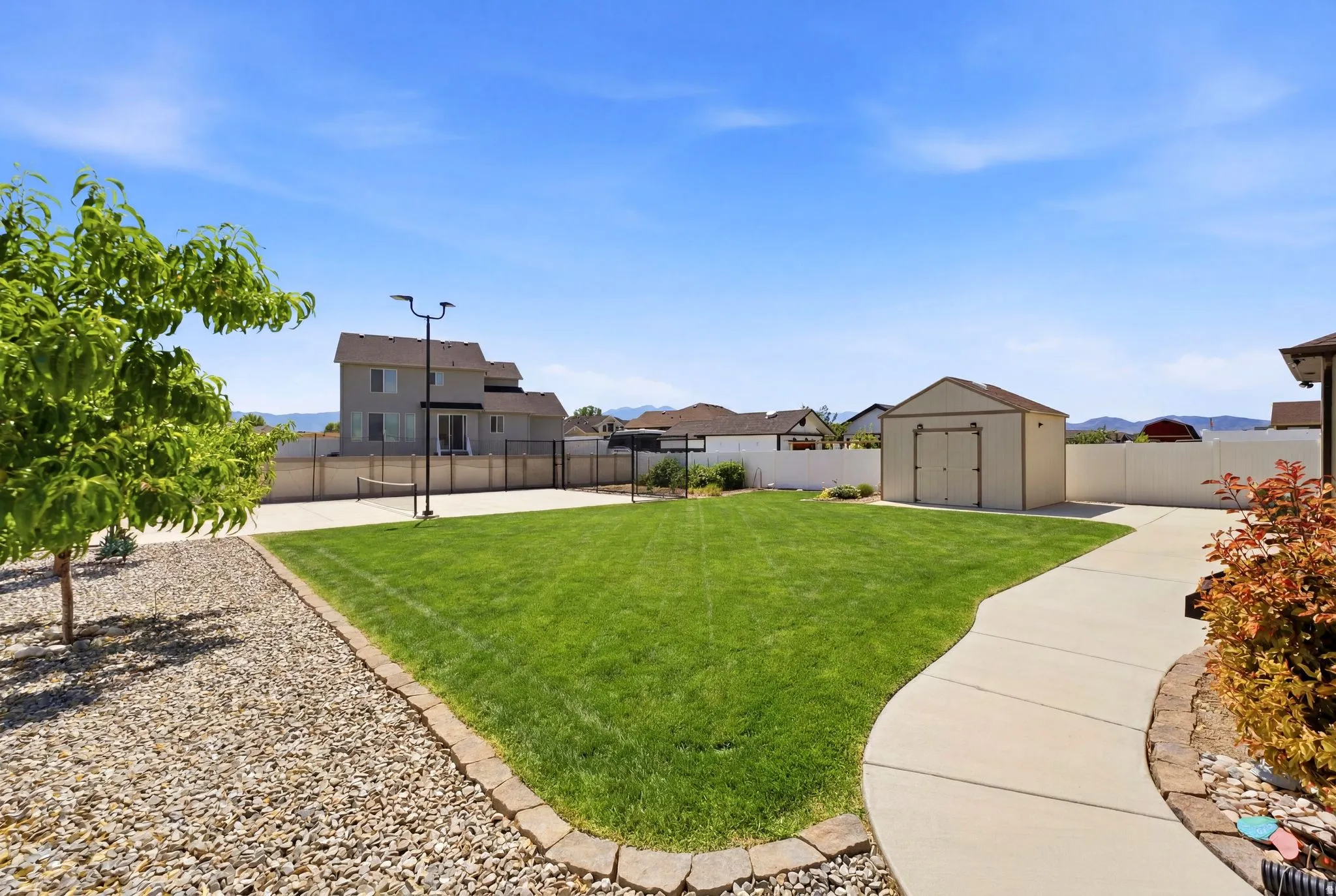 Expansive backyard featuring a manicured lawn, concrete patio, and a dedicated sport court