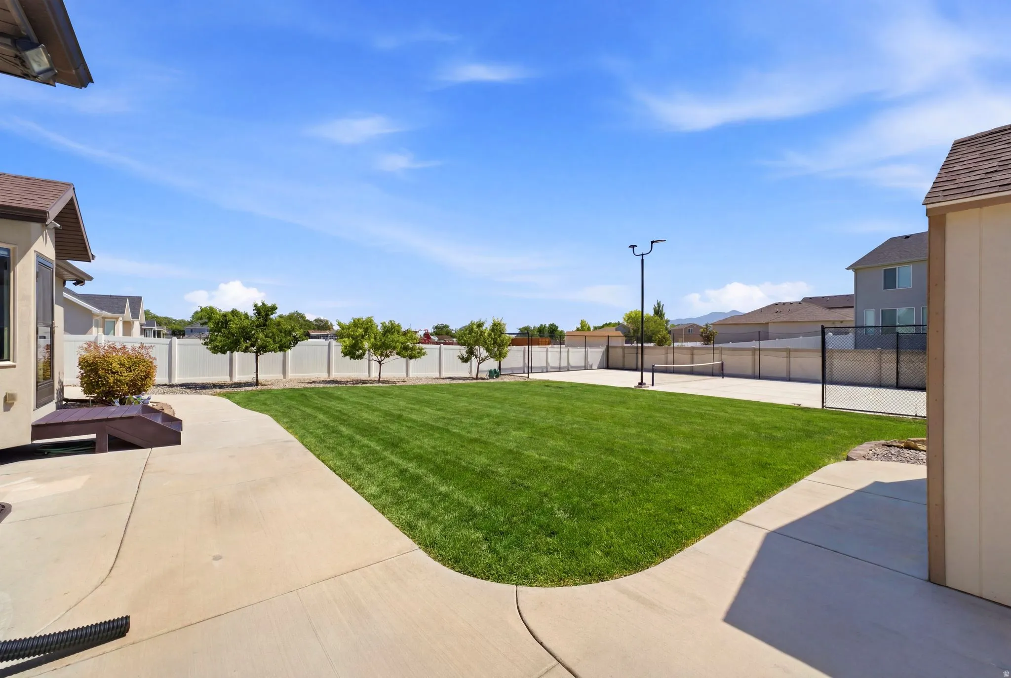 Expansive backyard featuring a large green lawn, a dedicated sport court with a net, and mature perimeter trees