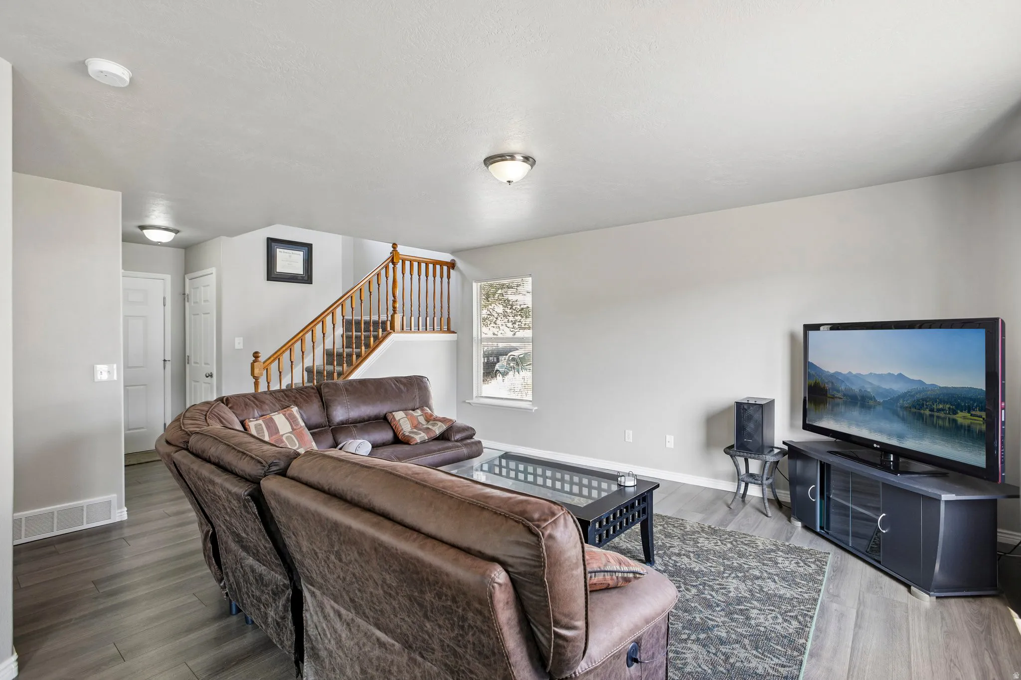 Open-concept living area featuring wood-finish flooring, a light gray color palette, and a prominent staircase with natural wood railings